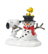 Woodstock sits back and enjoys the view as Snoopy puts the finishing touches on the most charming carrot-nosed snowman in Peanuts Village. By Department 56.